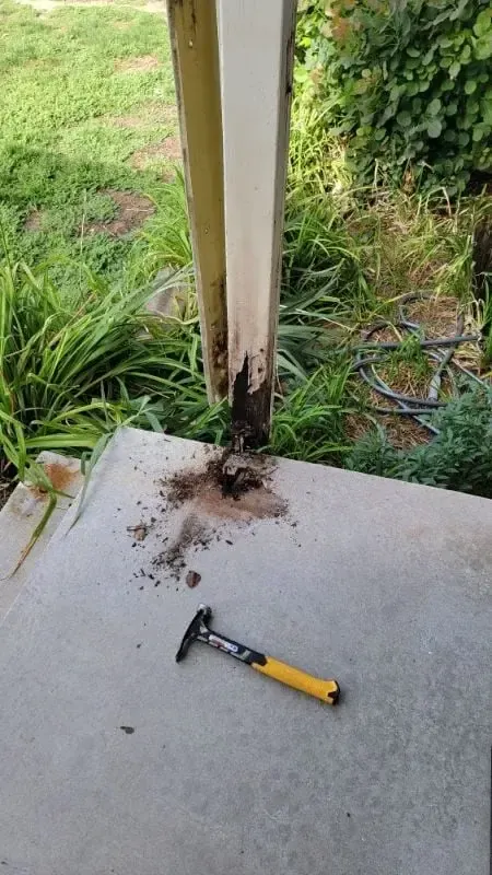 Rotted base of a wooden porch post on a concrete slab with a hammer beside it