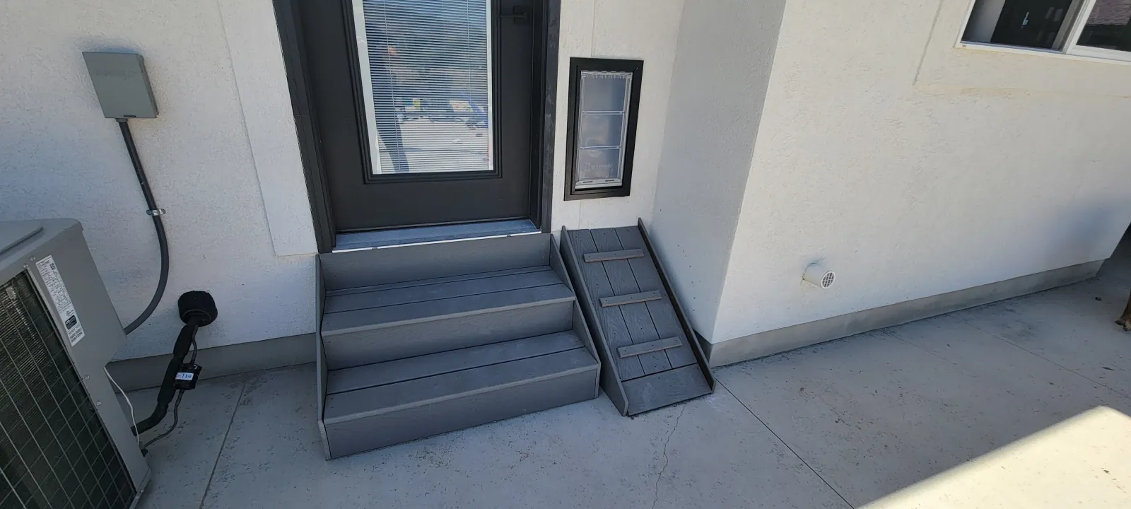 Exterior concrete entry with dark painted steps and a metal handrail