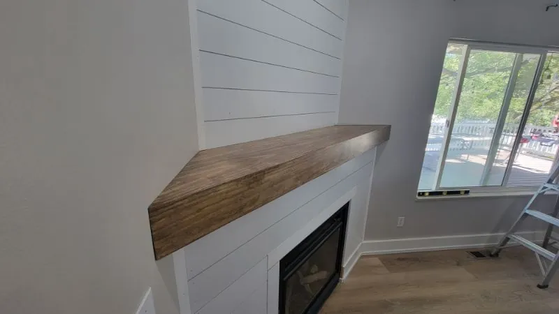 Shiplap fireplace wall with a thick wood mantel and windows alongside